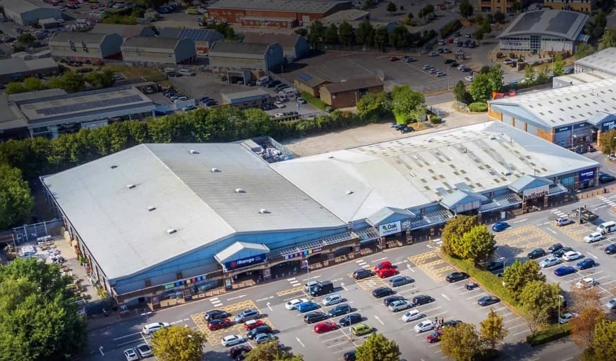 Aerial view of a large retail complex with multiple storefronts and a busy parking lot filled with cars.
