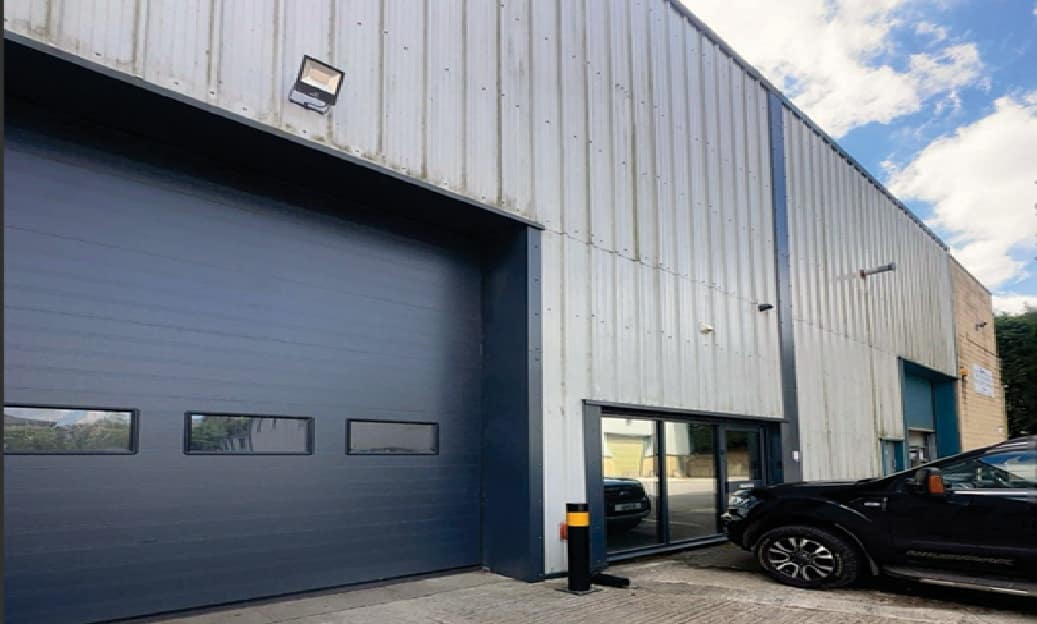 Industrial building with a large blue garage door, metal siding, and a black pickup truck parked outside.