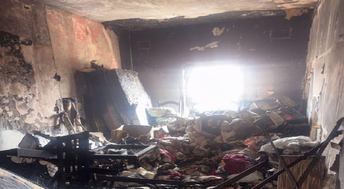 Charred, rubble-strewn room with piled debris and a bright window at the far end.