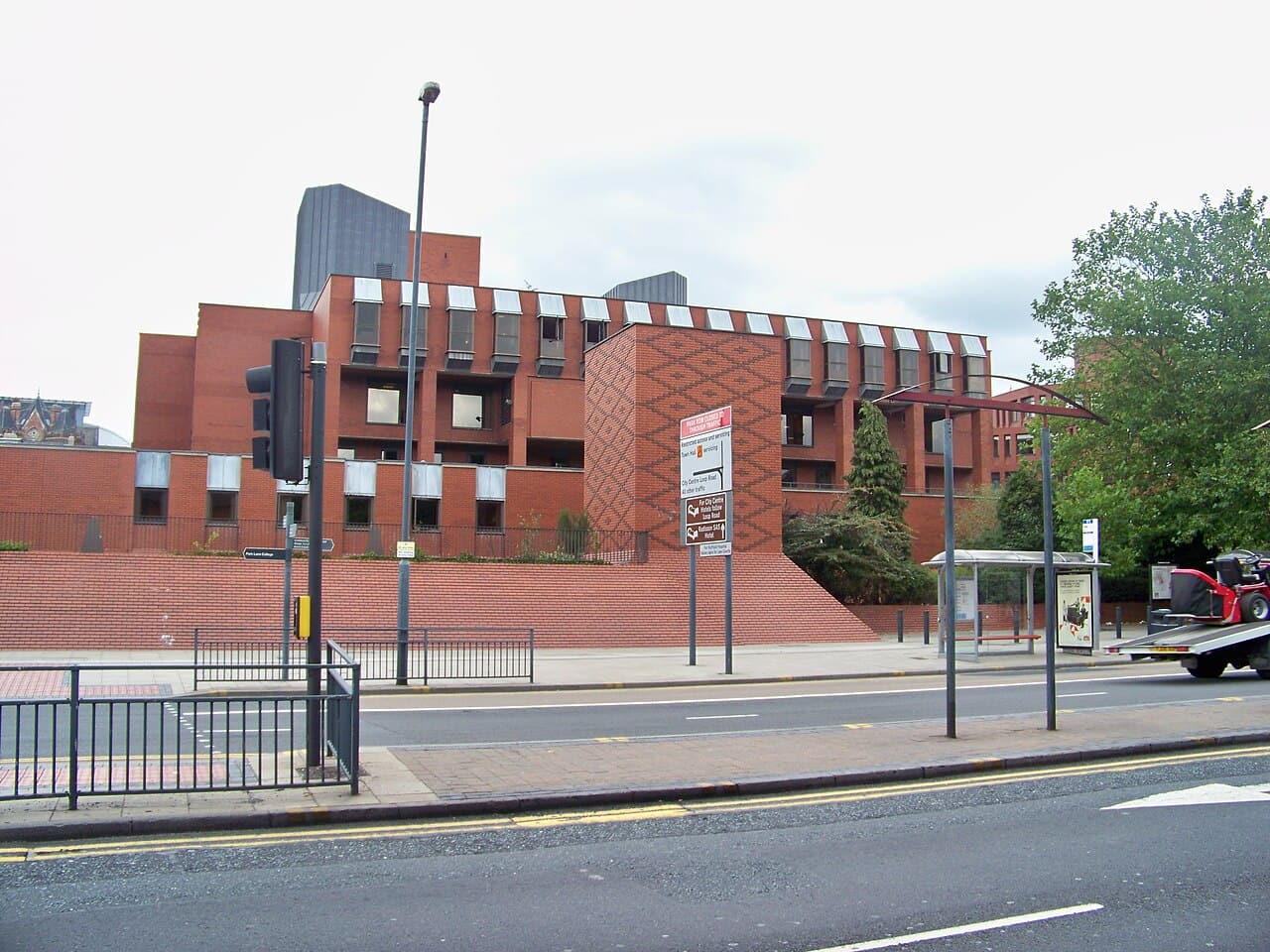 Red brick modern building along a city street with a decorative lattice brick wall and a bus stop in the foreground.