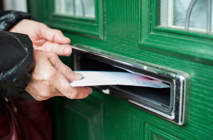 Person inserts a letter into a green mailbox slot on a doorhand close-up.