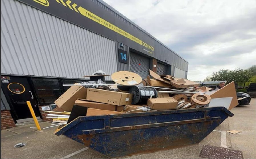Blue industrial dumpster overflowing with cardboard boxes and scrap material outside a warehouse loading bay labeled 14.